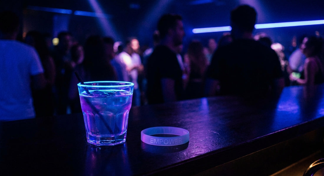 A cocktail glass on a nightclub bar counter with a test wristband placed beside it under moody blue and purple lighting.